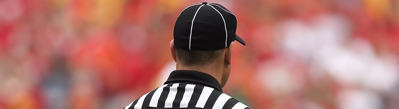 back of a referee wearing a striped black and white shirt and cap