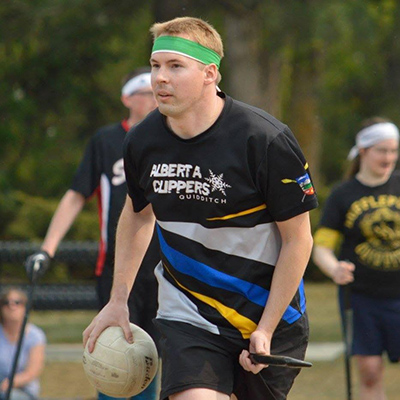 Brian Galloway wearing a black jersey, carrying a white quaffle on a broomstick